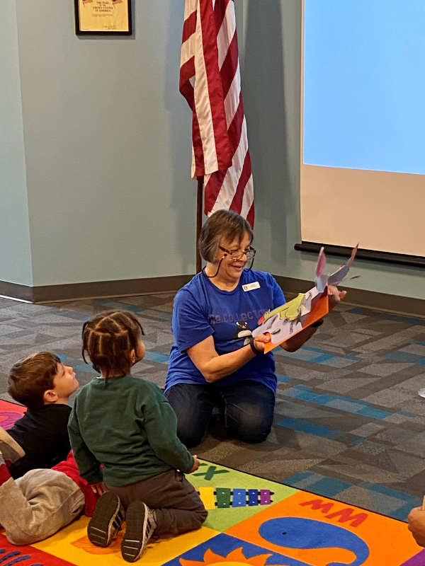 Librarian reads a pop-up book to two rapt children.